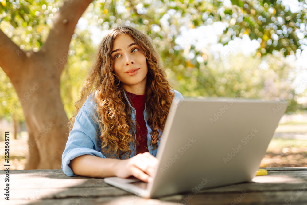 Attractive woman working or studying at the laptop as sitting in city park. Freelancer working in the park. Online course Attractive woman working or studying at the laptop as sitting in city park. Freelancer working in the park. Online course
