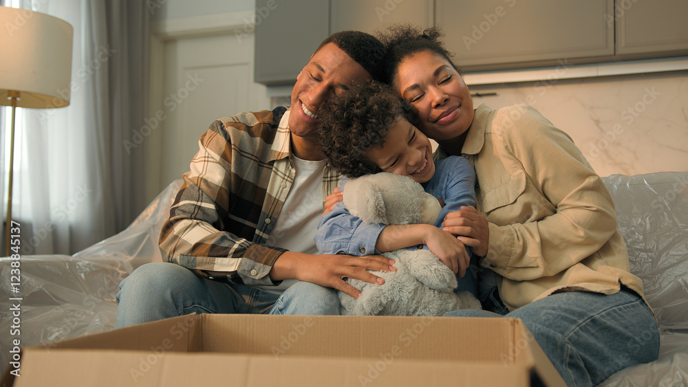 Little kid boy adopted child open cardboard box parcel surprise gift birthday present toy excited happy son hugging teddy bear parents children African American bonding love family at home moving day Little kid boy adopted child open cardboard box parcel surprise gift birthday present toy excited happy son hugging teddy bear parents children African American bonding love family at home moving day
