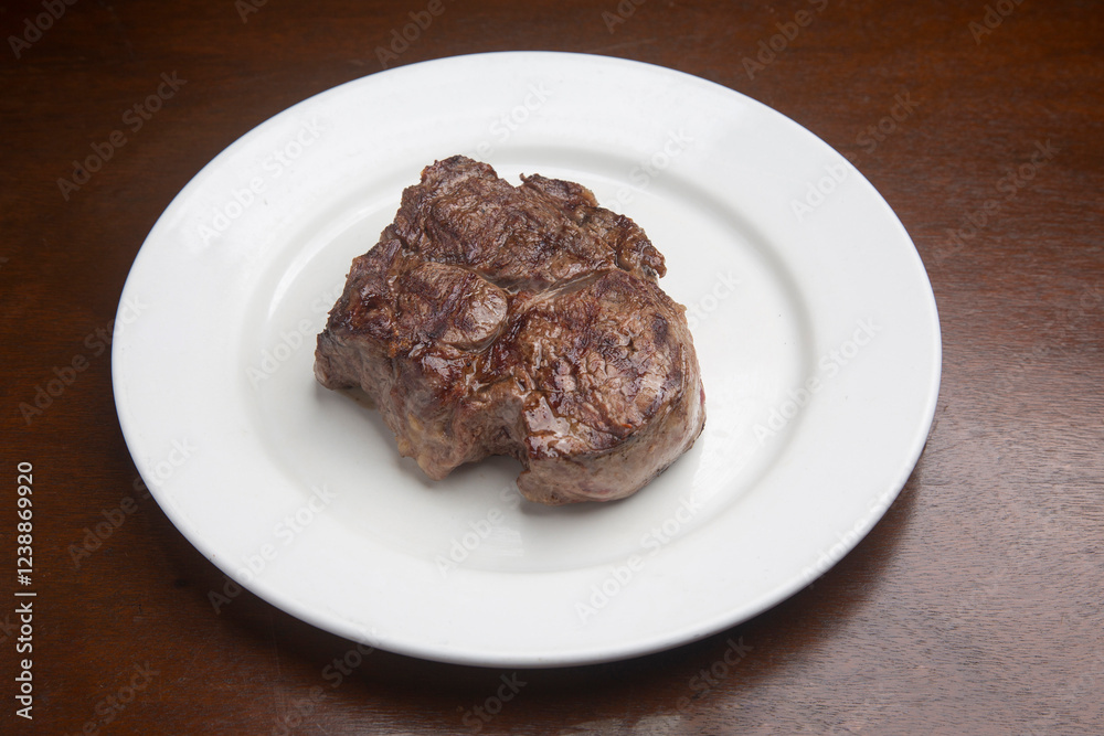 Grilled beef steak is presenting on a white plate on a wooden table Grilled beef steak is presenting on a white plate on a wooden table