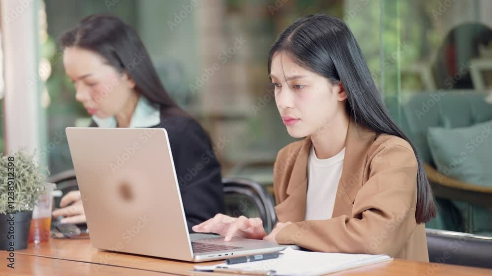 Two women are sitting at a table with a laptop in front of them. One of the women is looking at the laptop with a frown on her face