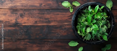 Fresh green herbs in a black bowl on a rustic wooden surface with scattered leaves and ample copy space for text photo