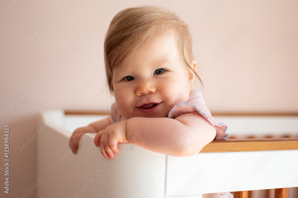 Cute Caucasian baby girl laughing standing in her crib. Portrait of laughing happy healthy 7 month old baby girl Cute Caucasian baby girl laughing standing in her crib. Portrait of laughing happy healthy 7 month old baby girl