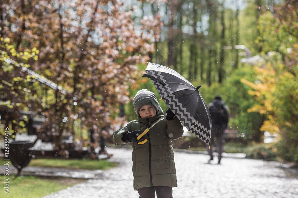 Fototapeta premium A small child of 5 years old with an umbrella in his hands during the spring rain. A spring break photo. A child under an umbrella.