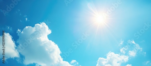 Bright clear blue sky with sun shining above fluffy white clouds ideal for backgrounds and designs Copy Space
