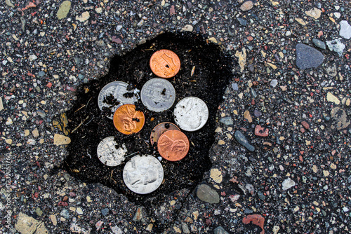 coins money in a pothole in the road abstract sunk costs unexpected costs metaphor bids infrastructure construction costs spending budget city planning roads background