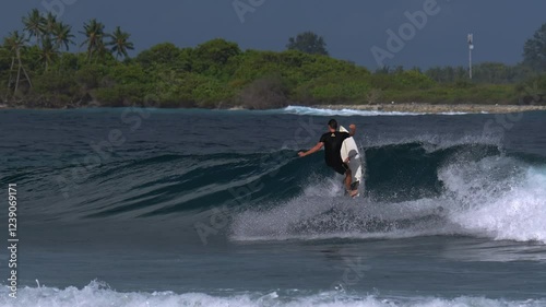 An adult male surfer catches a blue wave in the tropical waters of the Indian Ocean. A very hot sunny day.