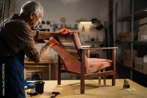 Fotografie elderly craftsman removing upholstery from vintage armchair