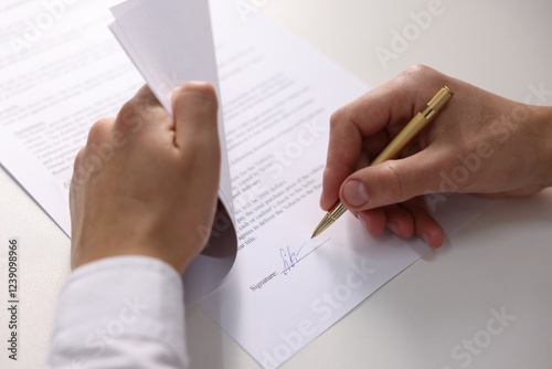 Man putting signature on document at white table, closeup
