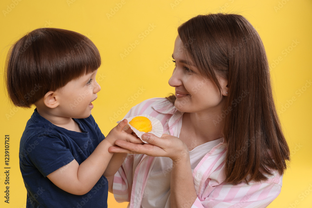 Mother and baby eating tasty mochi on yellow background Mother and baby eating tasty mochi on yellow background