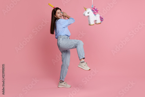 Fotografia Happy woman hitting unicorn shaped pinata with stick on pink background