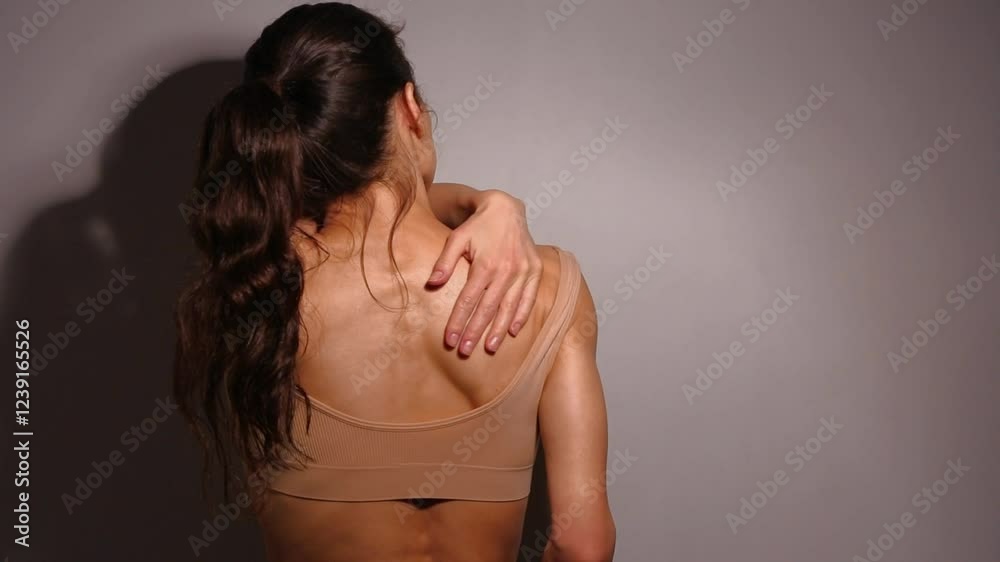 Beautiful woman massaging her hand the shoulder, neck, back view. Attractive body slim female model restoring in bra in studio low key light dark shadow wall background. Closeup relax beauty Beautiful woman massaging her hand the shoulder, neck, back view. Attractive body slim female model restoring in bra in studio low key light dark shadow wall background. Closeup relax beauty