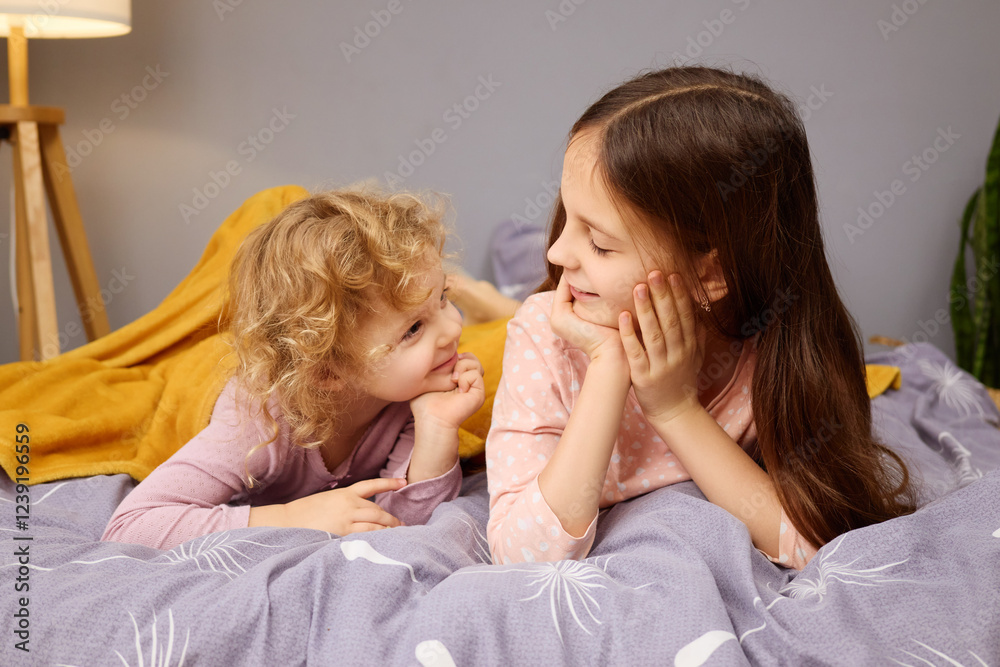 Two sisters share a joyful moment while lying on a comfortable bed covered with cozy blankets. The room is softly lit, creating a peaceful atmosphere for playful conversation Two sisters share a joyful moment while lying on a comfortable bed covered with cozy blankets. The room is softly lit, creating a peaceful atmosphere for playful conversation