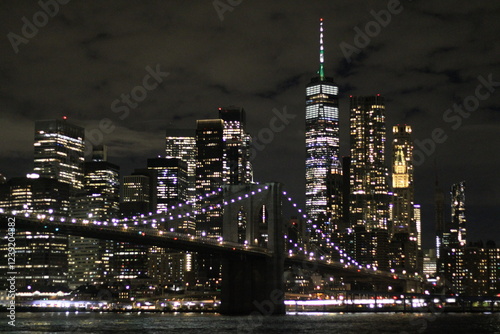 Nocny widok na Brooklyn Bridge i panoramę Manhattanu z DUMBO. Oświetlony most, refleksy w wodzie i tętniące życiem miasto tworzą niezapomniany klimat Nowego Jorku. photo