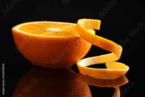 Fresh orange peel and half of fruit on black mirror surface, closeup