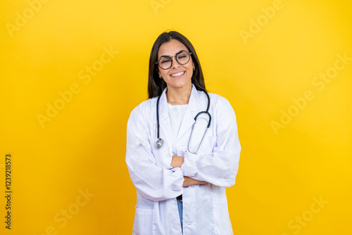 Young brunette doctor woman wearing stethoscope standing over isolated yellow background with a happy face standing and smiling with a confident smile showing teeth with arms crossed