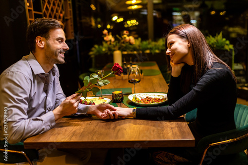 Loving boyfriend gifts a red rose to his girlfriend on a romantic dinner date.