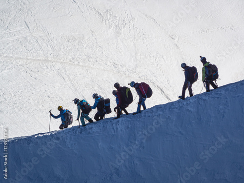 Paragliders with large backpacks with a parachute inside descend a steep snowy slope from the summit of the Aiguille du Midi to make a parachute jump. 