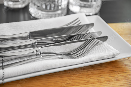 Obraz na płótnie A neatly arranged set of silverware, including polished forks and knives, rests on a folded white napkin atop a sleek plate. w salonie