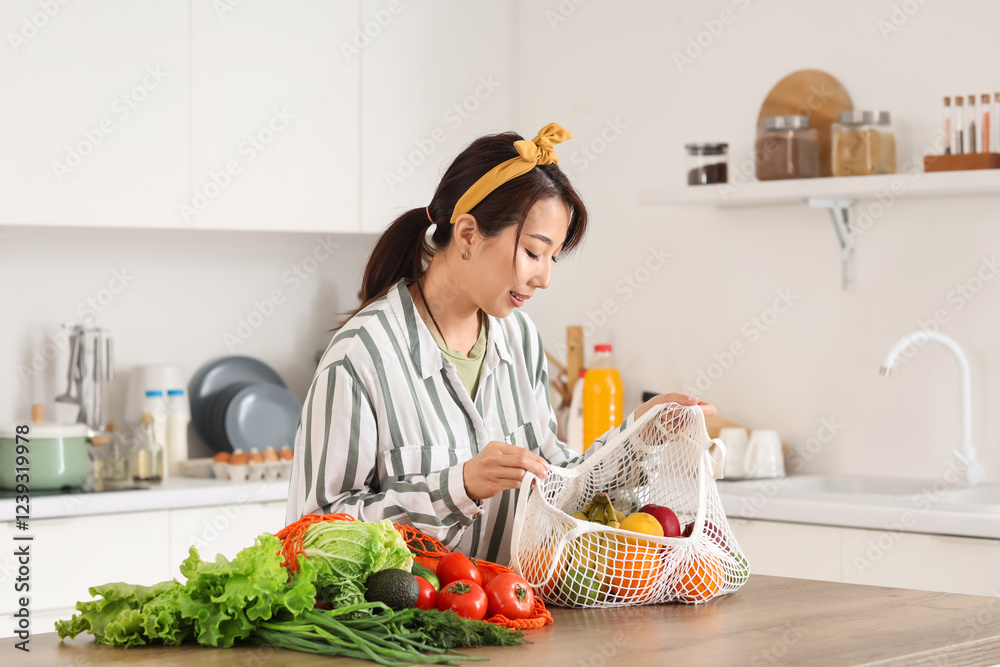 Young Asian woman unpacking fruits and vegetables from string bag onto counter in kitchen Young Asian woman unpacking fruits and vegetables from string bag onto counter in kitchen