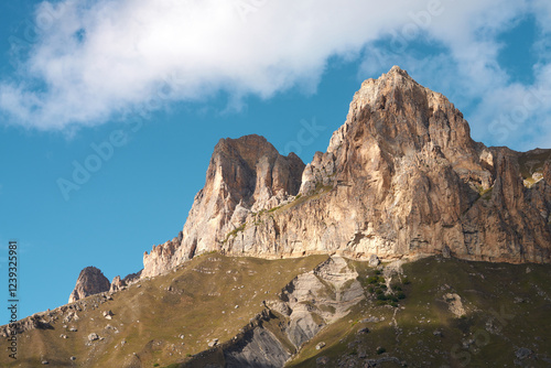 A rocky mountain peak against a blue sky with white clouds. High mountains of Kabardino-Balkaria. Copy space.