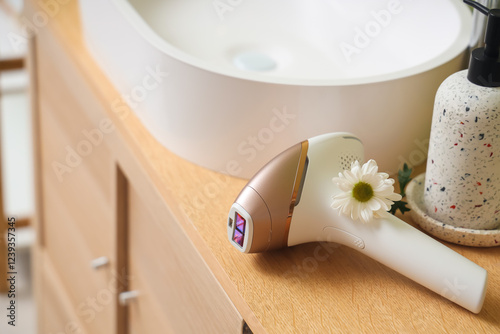 Modern photoepilator with flower on table near sink in bathroom photo