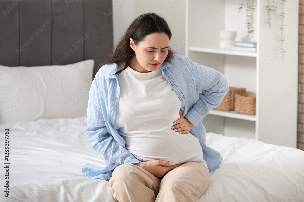Young pregnant woman suffering from back pain on bed in bedroom Young pregnant woman suffering from back pain on bed in bedroom