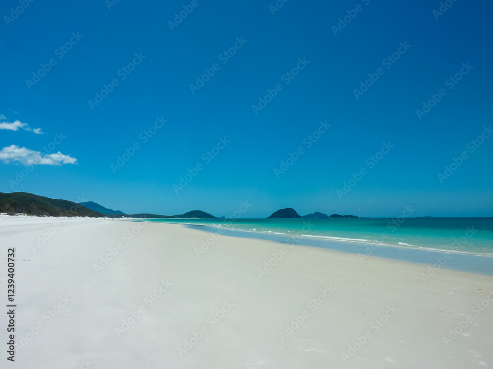 Pristine white sandy beach stretches along turquoise waters at Whitehaven Beach, Whitsunday Islands, Queensland, Australia. Gentle waves meet powdery silica sand. Vibrant blue sky. Summer vacation