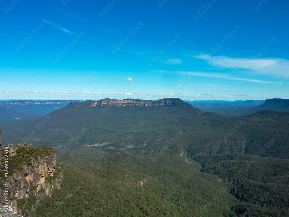 Fototapeta premium Panoramic view of Blue Mountains National Park in Australia. Deep valleys, dramatic sandstone cliffs, and eucalyptus forests under a pristine blue sky. Majestic mountain ranges stretching to horizon