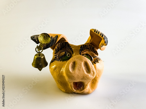 Funny clay figurine in the form of the head of a smiling pig with a bell in its ear on a white background. photo