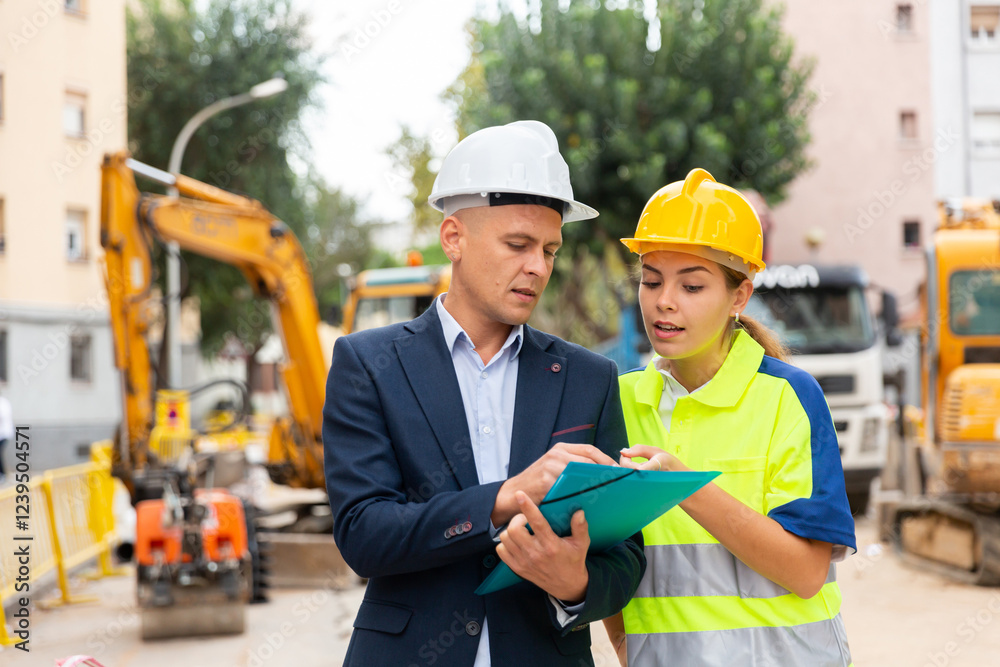 Foreman in suit and white hardhat discussing project documentation while staning in cosntruction area. Foreman in suit and white hardhat discussing project documentation while staning in cosntruction area.