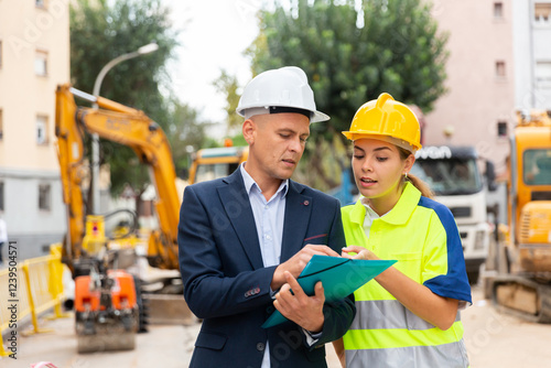 Foreman in suit and white hardhat discussing project documentation while staning in cosntruction area. photo