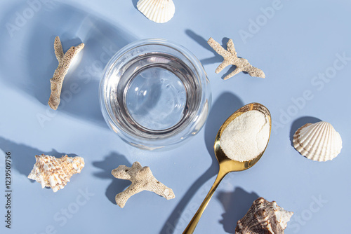 Marine collagen in golden spoon, glass of water and seashells on blue background