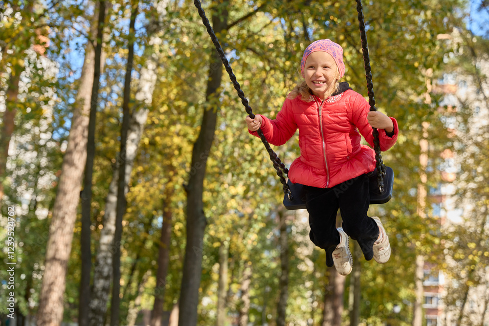 A laughing little girl is swinging on a swing on a sunny autumn day A laughing little girl is swinging on a swing on a sunny autumn day