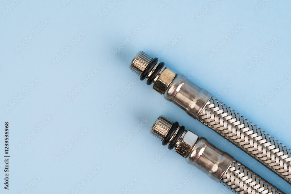 Braided stainless steel plumbing hoses with threaded connectors isolated on the blue background.