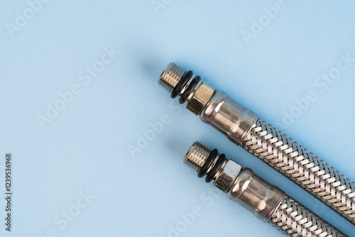 Obraz na płótnie Braided stainless steel plumbing hoses with threaded connectors isolated on the blue background. w salonie