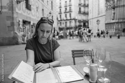 Young woman thoughtfully reads a menu at a charming European street cafe, enjoying the summer atmosphere.