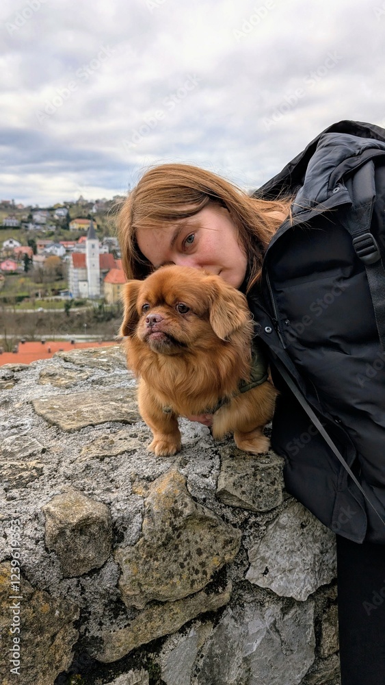 Portrait of pretty woman and cute little brown dog with Krapina city in background, pets and animals