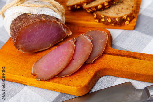 Appetizing sliced jerky boneless pork tenderloin served with toasted grain bread on wooden background. Meat snack.. photo