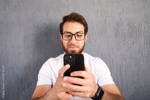 Fotografía de frente de joven apuesto con barba usando su teléfono celular.  