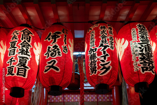 Illuminated red Japanese lanterns with elegant black calligraphy hang festively under a red ceiling.