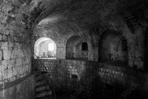 Obraz na płótnie A descending stone staircase leads into a dimly lit, historic underground passage with arched alcoves. w salonie