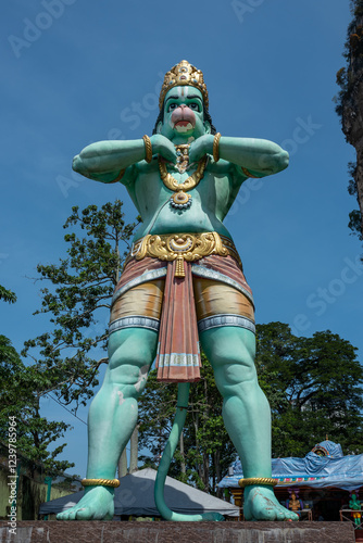 Majestic Teal Hanuman Statue Stands Tall Against a Vibrant Blue Sky, Adorned in Gold Accents and Traditional Attire. photo