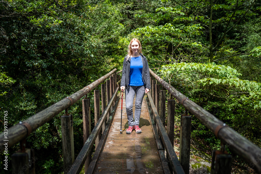 Smiling woman takes a leisurely hike across a rustic wooden bridge, deep within a vibrant green forest. Smiling woman takes a leisurely hike across a rustic wooden bridge, deep within a vibrant green forest.