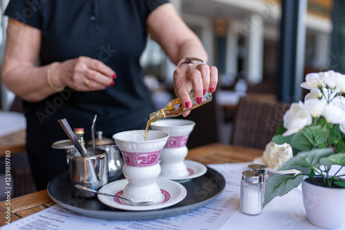 Waitress pouring flavored syrup into a traditional coffee cup at an outdoor cafe, adding a touch of sweetness.