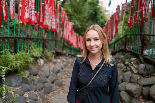Obraz na płótnie A cheerful woman walks on a scenic path adorned with vibrant red flags at a Japanese temple, enjoying a moment of serene travel. w salonie
