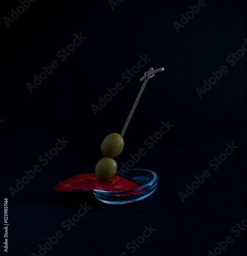 Conceptual image of a tomato and olive canape on a black background, gourmet food