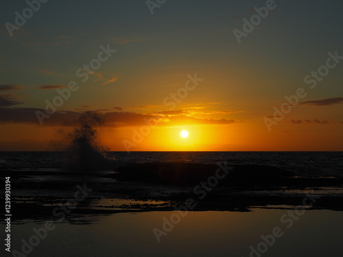 beautiful sunrise over the horizon at Tamarama beach in sydney, australia with a wave splashing against the rocks