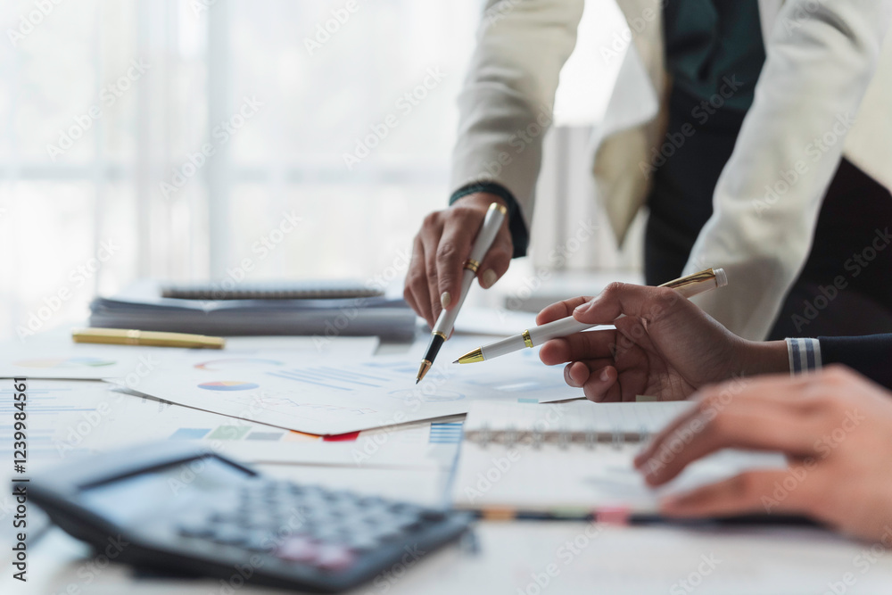 Business people analyzing financial charts and graphs using pens and calculator Business people analyzing financial charts and graphs using pens and calculator