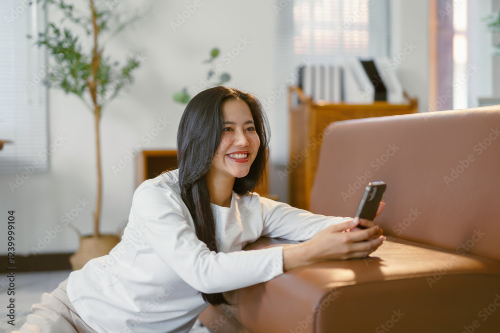 Young woman using smartphone and smiling while relaxing on floor at home Young woman using smartphone and smiling while relaxing on floor at home