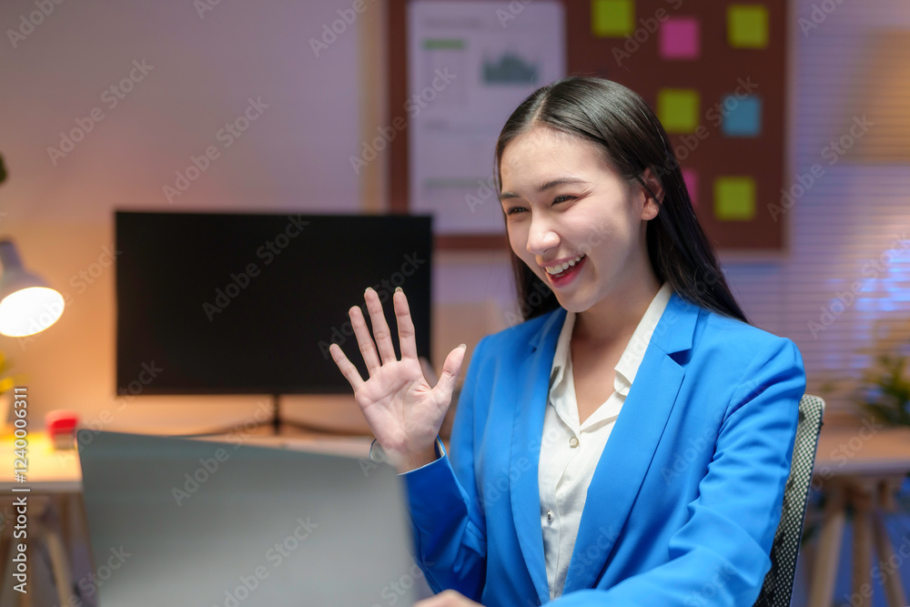 Asian businesswoman waving during a video call in her office at night Asian businesswoman waving during a video call in her office at night
